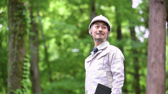 公園などでヘルメット姿でタブレットで点検する林業や施工管理などの現場作業員のポートレート安全管理とDX業務　カメラ目線上半身クローズアップ動画