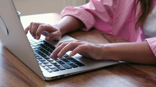 Close-up shot of a person's hands diligently typing on a laptop keyboard at a warm wooden desk. Perfect for illustrating productivity, remote work, online learning, or digital communication concepts