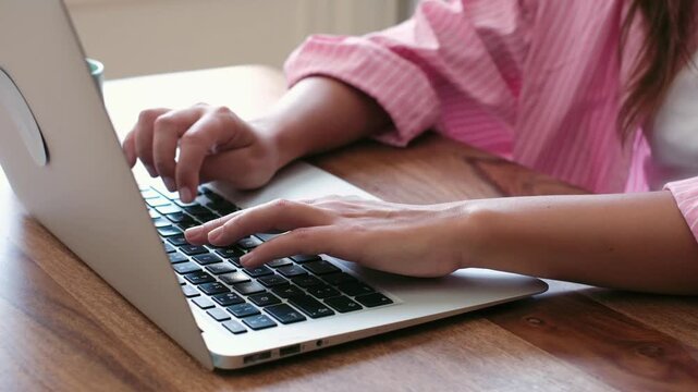 A close-up shot of a woman's hands typing efficiently on a laptop keyboard, highlighting productivity, digital work, and focused activity on a wooden desk.