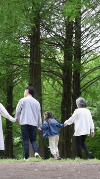 三世代家族の新緑の公園で手を繋ぐ歩く幸せなファミリーライフ動画スローモーション　全身顔無しの後ろ姿縦動画
