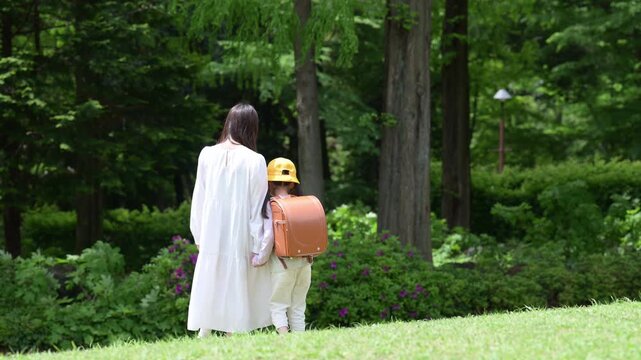 新緑の公園を手をつないで歩く母親とランドセル姿の女の子 親子の登校風景笑顔でかわいいスローモーションの動画　顔無しの後ろ姿