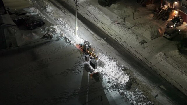 Cinematic drone aerial shot: snowplow removes accumulated snow from residential streets in Beechville suburb of Halifax after heavy snowstorm. Nova Scotia, Canada, overnight winter road clearing 4K