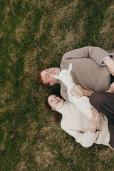 Fototapeta premium Cheerful couple outdoors, lying on grass with a goat kid nearby, warm sunlight, relaxed posture, candid moment, rustic setting, natural tones, gentle breeze, wholesome lifestyle scene