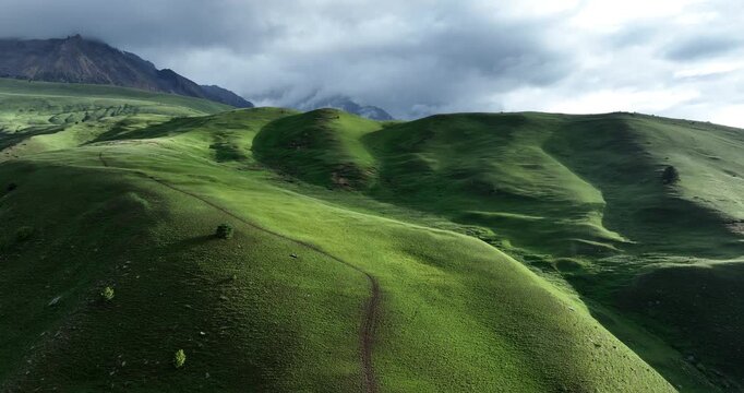 Trail in green grassland leading to snow capped mountain top landscape in the fog