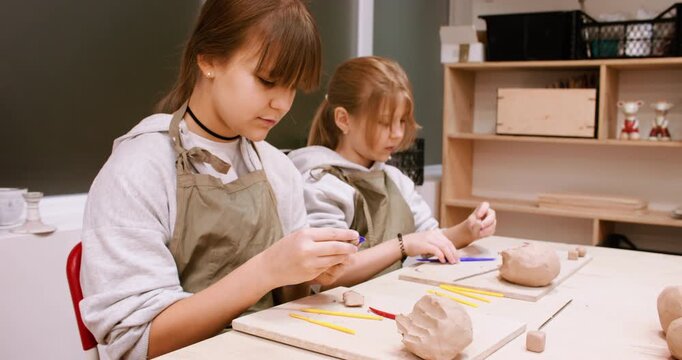 Clay modeling. Ceramic workshop. Two creative kids girls molding handmade raw using color tool in pottery artisan art professional studio.