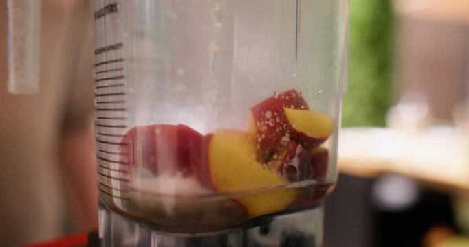 Pouring water blender. Fruit drink preparing. Fresh peaches pieces in automatic machine covering with alcohol syrup liquid in bar.