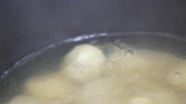 Cinematic close-up of potatoes boiling in bubbling water with steam
