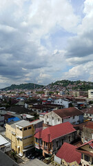 Fototapeta premium High-angle view of a densely populated city residential area with colorful rooftops, set against green hills and a dramatic cloudy sky. Great for travel and demographic themes.