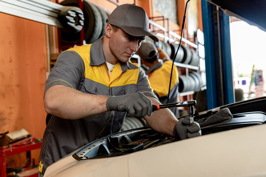 Mechanic using wrench while working on car engine at garage workshop