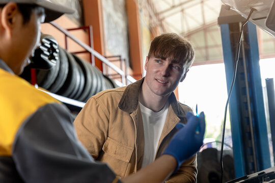 Young car owner talking with mechanic in auto repair shop.