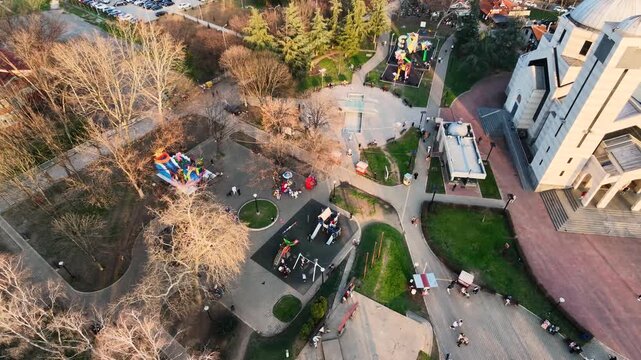 Drone aerial of Nis Serbia with apartment buildings and an open air market visible against a hazy orange sunset sky and surrounding hills in the distance
