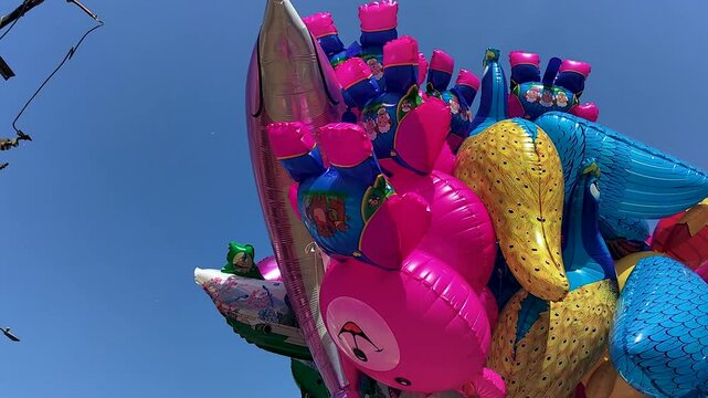 Bright inflatable animal balloons sold by street vendor under blue sky. Ideal for festival promos, childhood themes, street market visuals, and colorful lifestyle content.