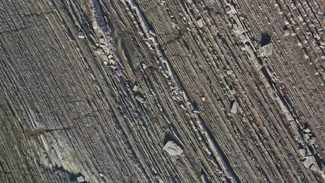 Incredible aerial top down view showing the unique flysch rock formations of Sakoneta beach, revealing geological strata as the camera moves towards the gentle waves of the Atlantic Ocean