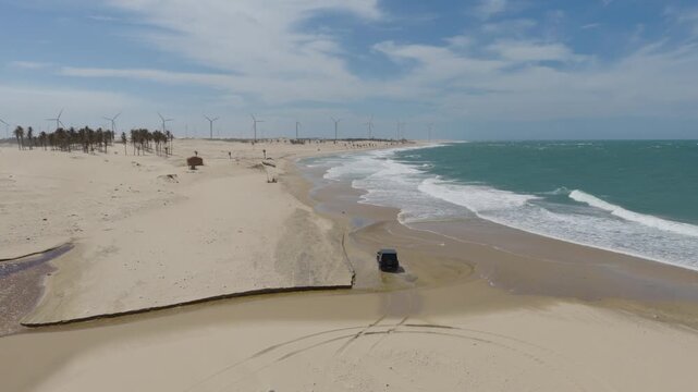 4x4 vehicle driving through shallow lagoon into Atlantic surf along Taiba beach in Sao Goncalo do Amarante municipality, Ceara state, Brazil, South America with wind farm in background under clear sky