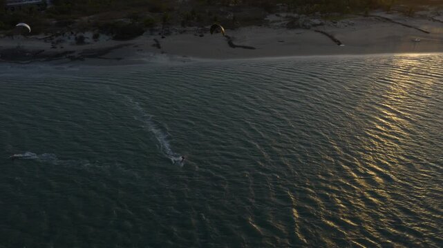 Kitesurfer riding across textured water near Ilha do Guajiru in Itarema municipality, Ceara state, Brazil, South America during golden sunset light with long shadows and wind patterns drone tracking