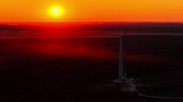 Vibrant red sunset over a silhouetted industrial tower in a misty valley
