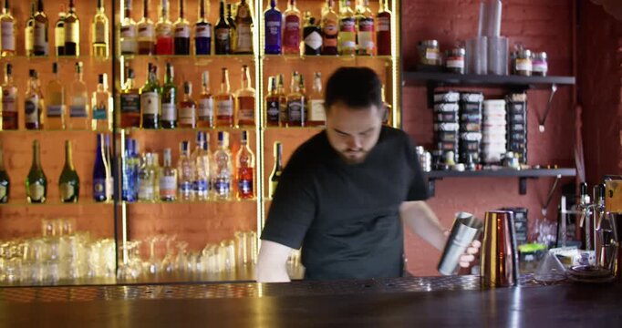 Cocktail making. Barman working. Bearded male skillfully putting ice cubes using metal scoop shaker cup in restaurant.