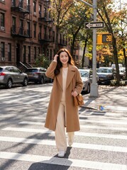 Obraz premium A stylish woman wearing camel coat walks across Manhattan zebra crossing near brownstone apartments on crisp autumn day with long shadows and vibrant yellow signals