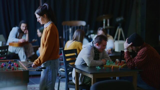 Students are engaged in various games, including foosball and board games, on a university campus. This inclusive group enjoys leisure time together, fostering friendship and social interaction.