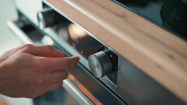A hand operates the temperature dial of an oven in a kitchen setting. This action emphasizes the process of preparing food for baking or cooking