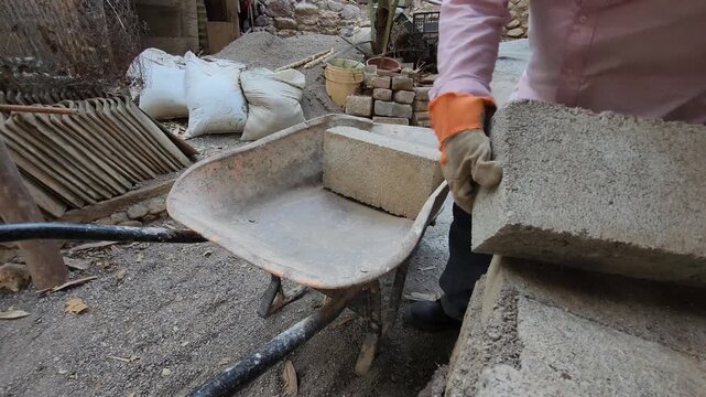 Worker Loading Heavy Concrete Block into Wheelbarrow