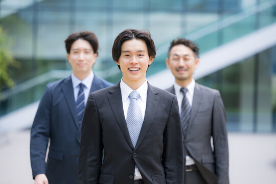 笑顔で歩くスーツで新卒採用や新人の若手ビジネスチームのポジティブ(前向き)なイメージ　転職や就活、採用などのカメラ目線の笑顔複数の横並び