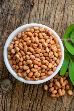 Raw peanuts in white bowl with green leaves on rustic wooden background