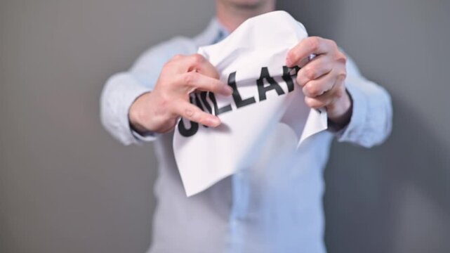 A man in a light shirt shows a sign that states collapse. He then manipulates the paper, crumpling it and shaking it, illustrating the concept of collapse in an indoor setting