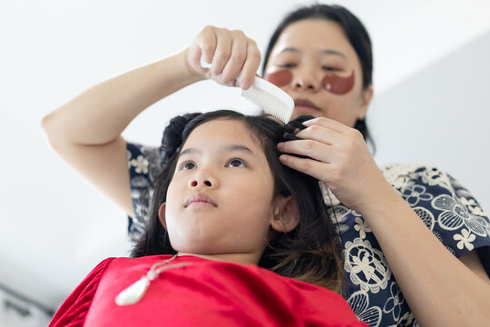 Mother Combing and Styling Her Daughter's Hair into Buns for an Event
