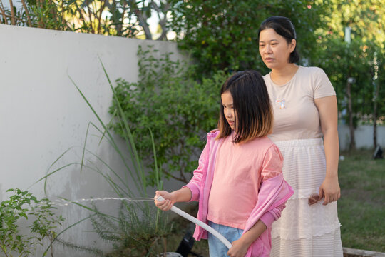 Asian Mother and Daughter Watering Plants in the Garden Together