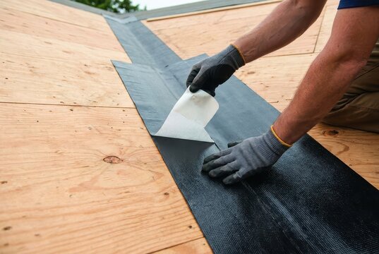 Construction worker installing waterproof membrane on a wooden roof deck for weather protection.