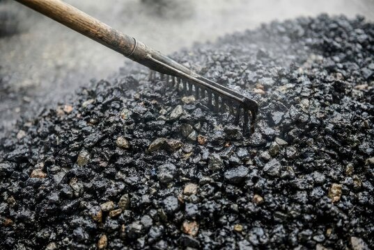 Close-up of a rake smoothing hot asphalt, with steam rising from the construction material.