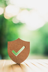 Wooden shield icon with check mark on natural bokeh background. Concept of protection, security, insurance, and guaranteed safety for business and home. High quality professional stock photo. © sommart