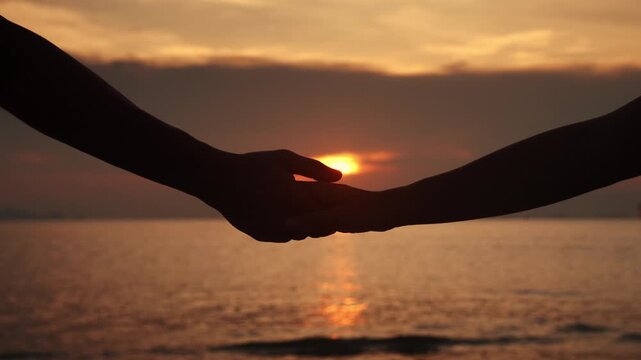 Close up man in love hesitantly holds out his hand, a woman takes his hand on a romantic date, on background of sunset on the sea. Concept of mutual sympathy is declaration of love.