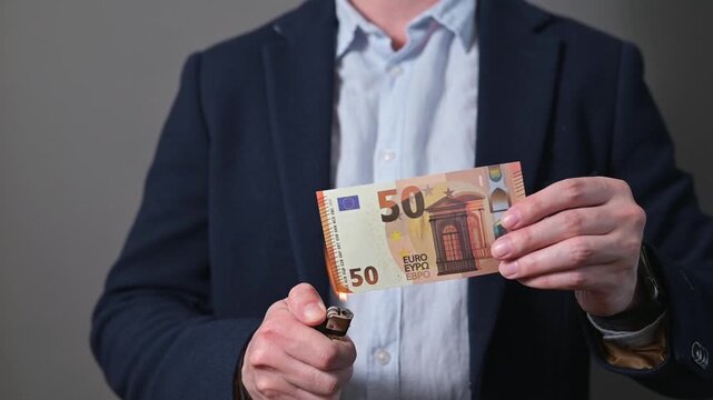 A person holding a banknote euro lights one edge with a lighter, creating flames. This setting captures the action of burning money, focusing on the interaction between the individual and the banknote
