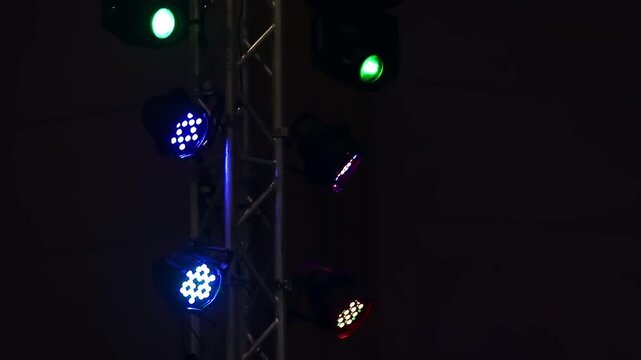 Colorful LED spotlights hanging on a metal truss tower blinking and shining in the dark. Concert stage lighting and entertainment event background concept.