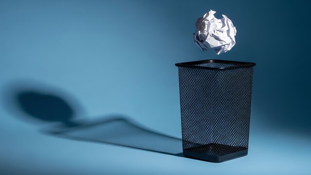 Discarding a crumpled paper ball into a trash can with a shadow on a blue background