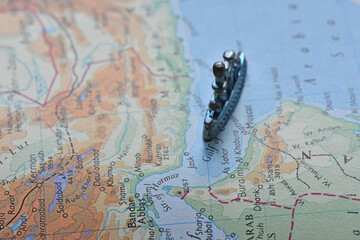 High-angle selective focus shot of a toy battleship on a vintage map, navigating the Strait of Hormuz and Gulf of Oman, depicting maritime military strategy and regional geopolitics. © IbrahimAlkan