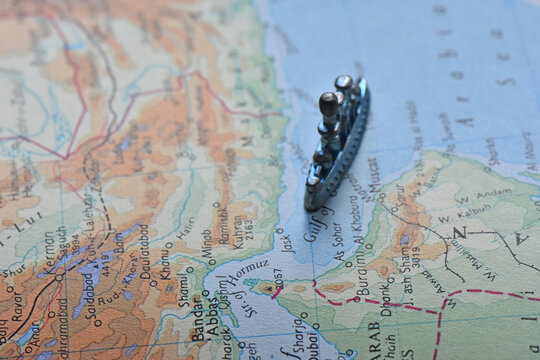 High-angle selective focus shot of a toy battleship on a vintage map, navigating the Strait of Hormuz and Gulf of Oman, depicting maritime military strategy and regional geopolitics.