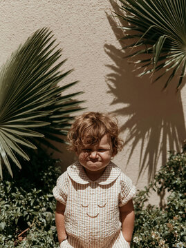 Funny toddler making a grumpy face in summer sunlight with palm leaves shadows