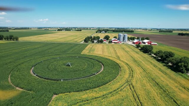 Aerial view of expansive farmland with a circular irrigation system, silos, and red-roofed barns