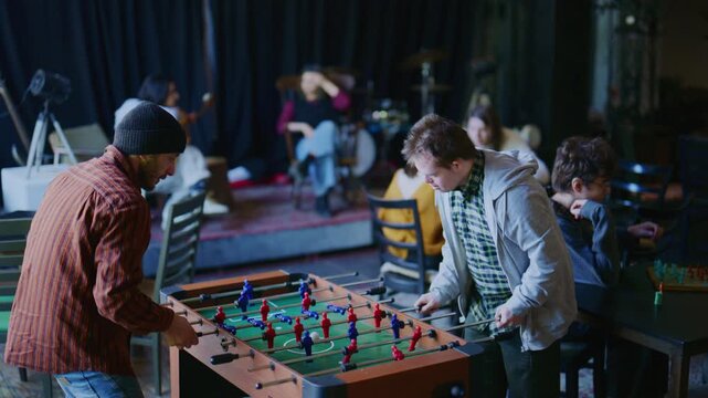 Young men, including one with Down syndrome, enjoy a game of foosball. They share a friendly and inclusive recreational activity.