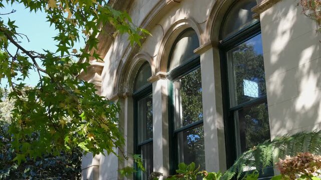 Ornate arched windows on a historic Victorian-era heritage building in Australia, lush deciduous trees. Quiet moment and garden foliage in dappled sunlight. Werribee Mansion, Melbourne, Australia
