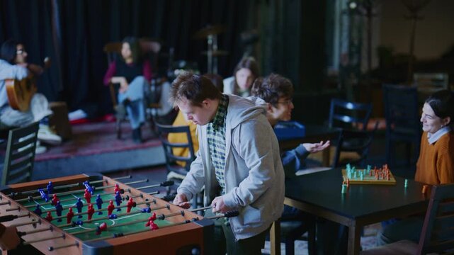 A diverse group of students enjoys playing foosball and board games in a relaxed setting. Young people, including a student with Down Syndrome, engage in fun activities and connect.