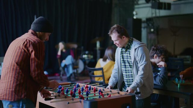Two happy young students, one with Down Syndrome, play an exciting game of foosball. They share a moment of joy and high-five, showcasing friendship and inclusion.
