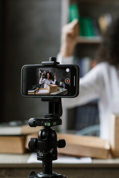 A woman excitedly records herself unboxing a package while filming with her smartphone on a tripod, showcasing a modern content creation setup