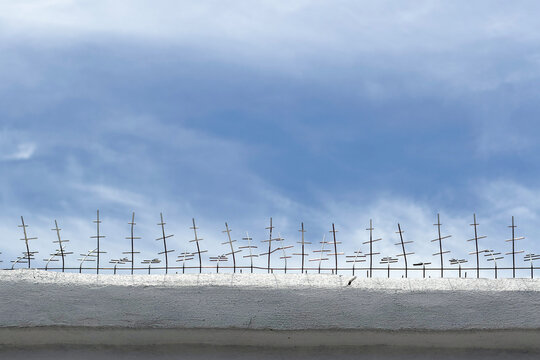 Anti-bird spikes installed on a white concrete wall against a blue cloudy sky.