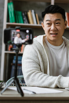 A man is actively engaged in recording a video using his smartphone and laptop, likely for online content creation or a virtual meeting