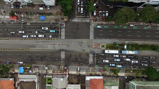 Aerial Top View of Busy City Crossroads with Traffic Flow. High Angle Shot of Metropolitan Intersection featuring TransJakarta Buses, Cars, Motorcycles, Zebra Crossings, and Modern Urban Infrastructur