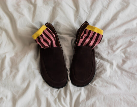 Brown women's suede loafers and striped pink socks on a light background, top view
